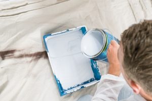 Professional painter pouring paint in a tray with drop cloths down
